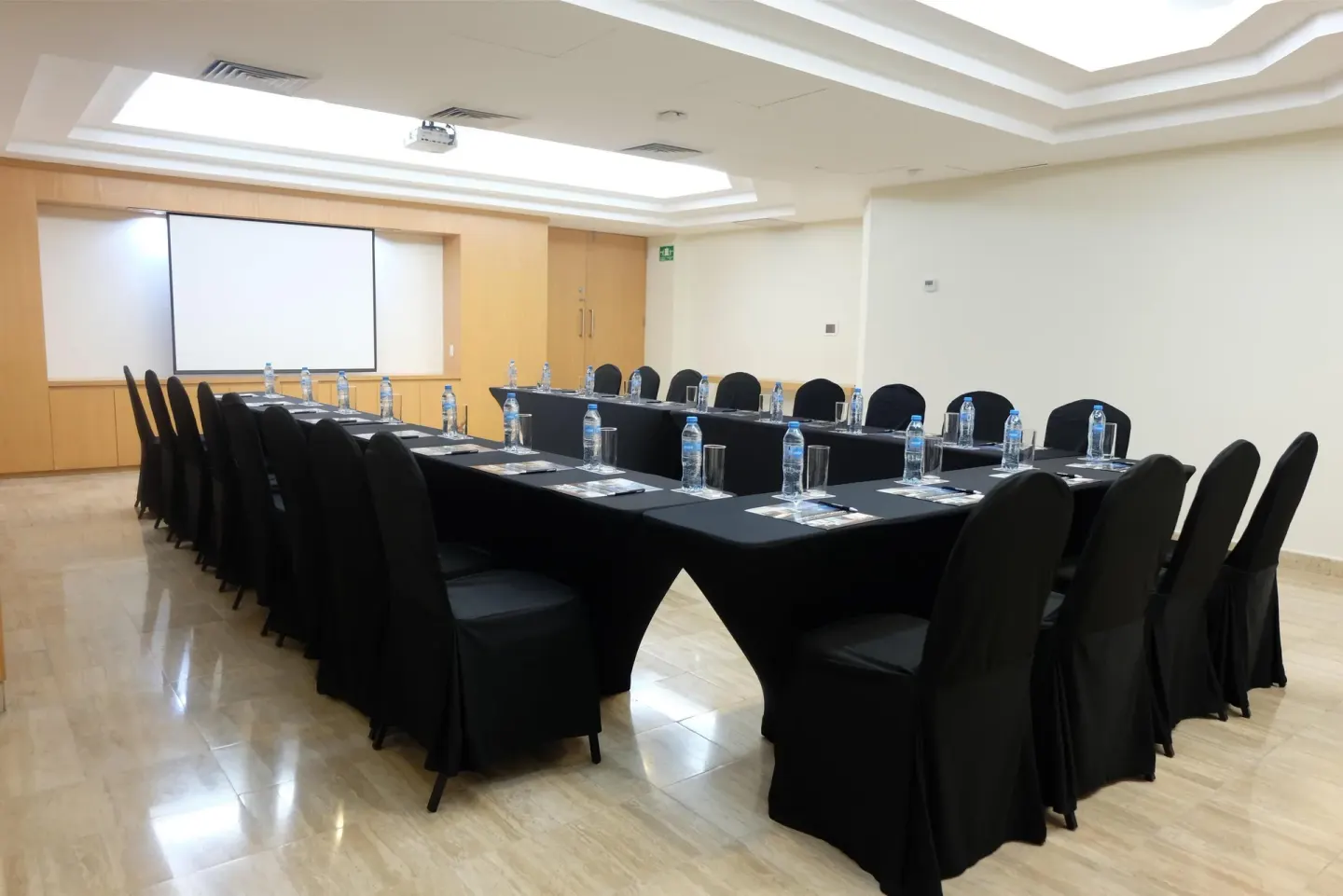 Meeting room with black-covered tables, chairs, and projection screen at Oasis Palm.