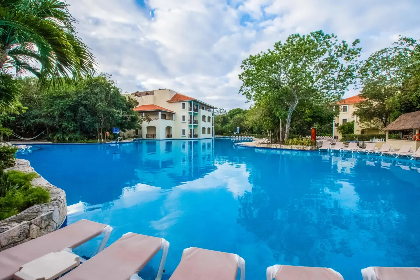 Large blue pool with resort buildings and loungers at Occidental at Xcaret Destination.