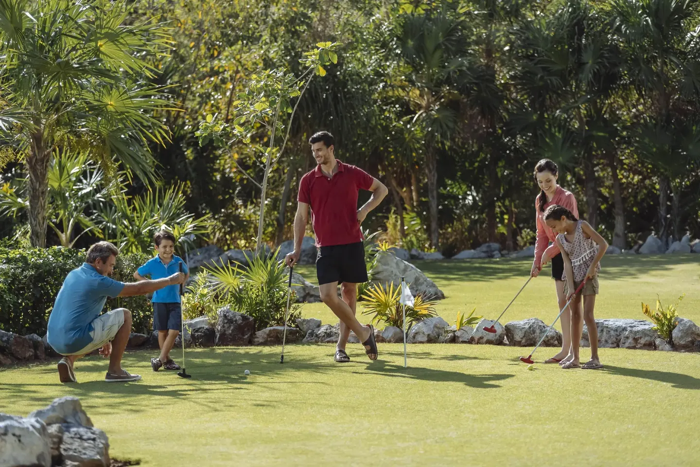 Family playing mini golf on tropical grounds at Occidental at Xcaret Destination.