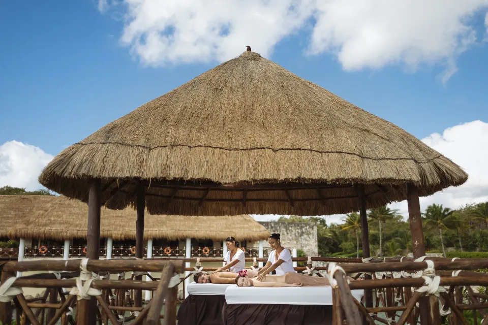 Outdoor massage tables beneath a thatched palapa at Occidental at Xcaret Destination.