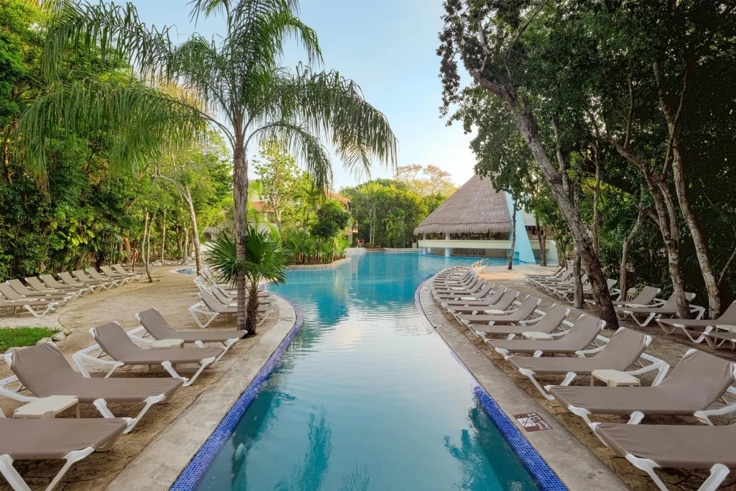 Narrow pool channel lined with loungers at Occidental at Xcaret Destination.