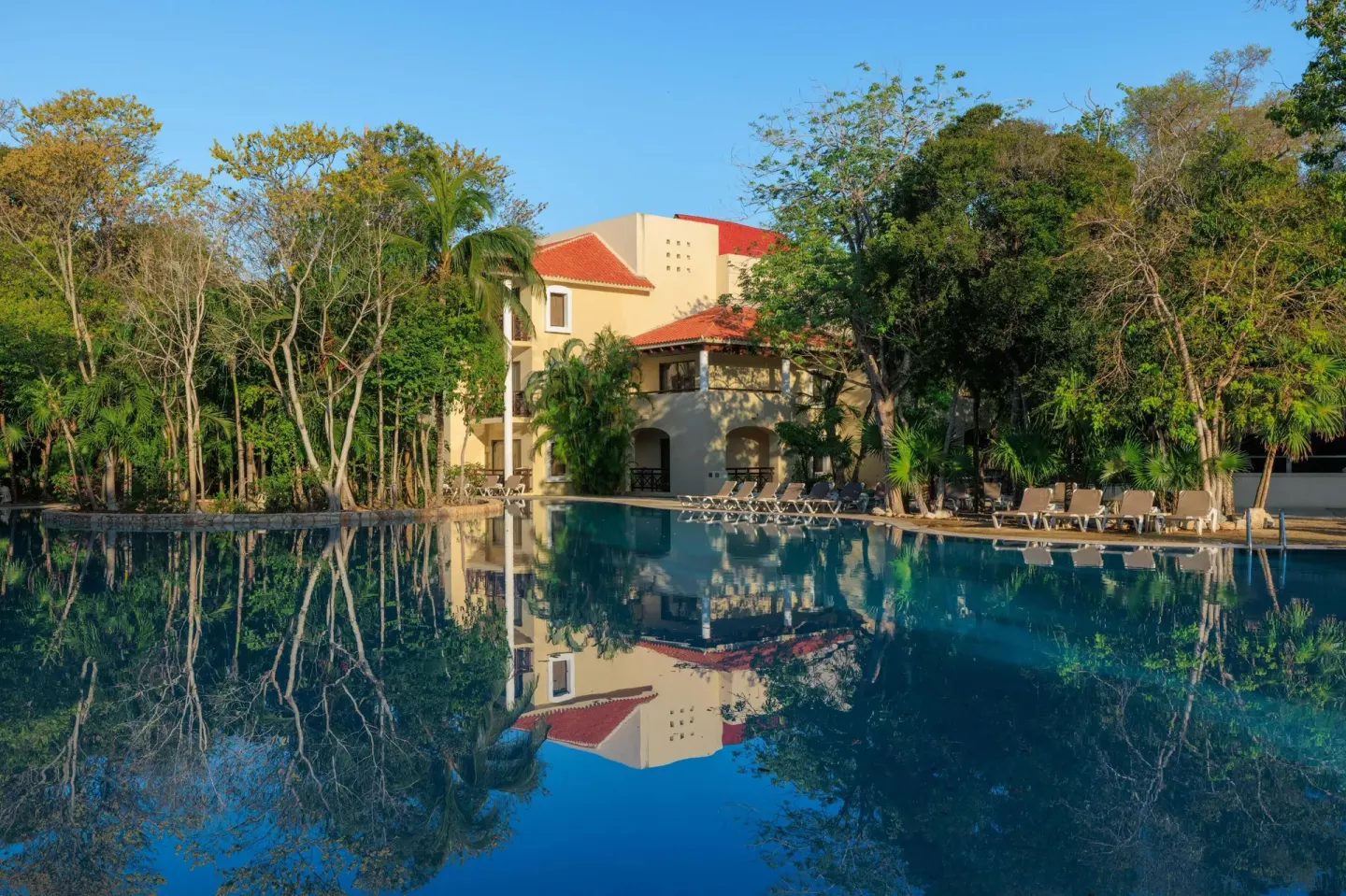 Pool reflecting trees and a red-roof resort building at Occidental at Xcaret Destination.