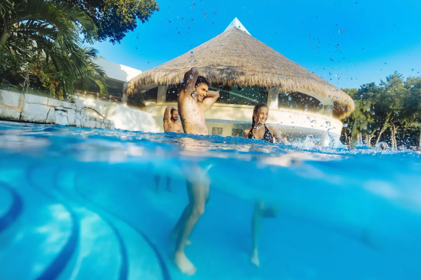 Guests splash in a pool beneath a thatched roof at Occidental at Xcaret Destination.