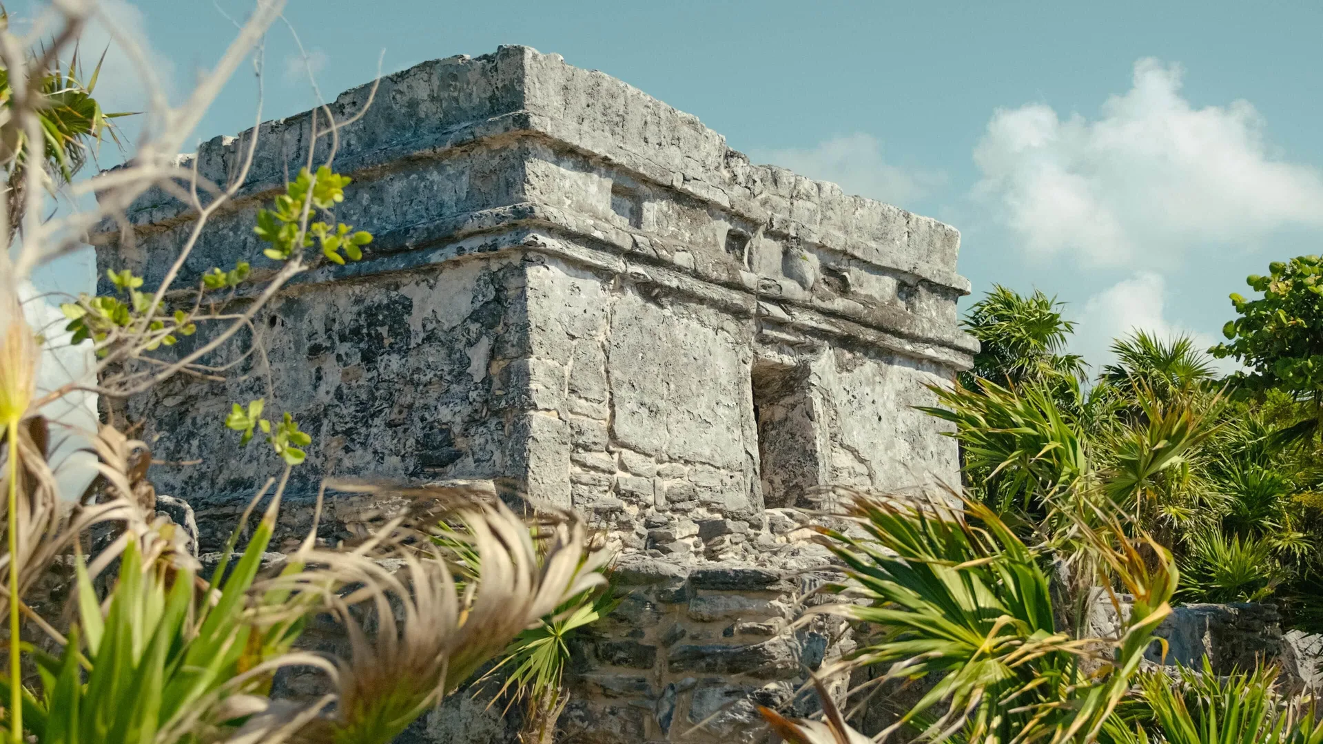 A small stone ruin stands among coastal plants at Occidental at Xcaret Destination.