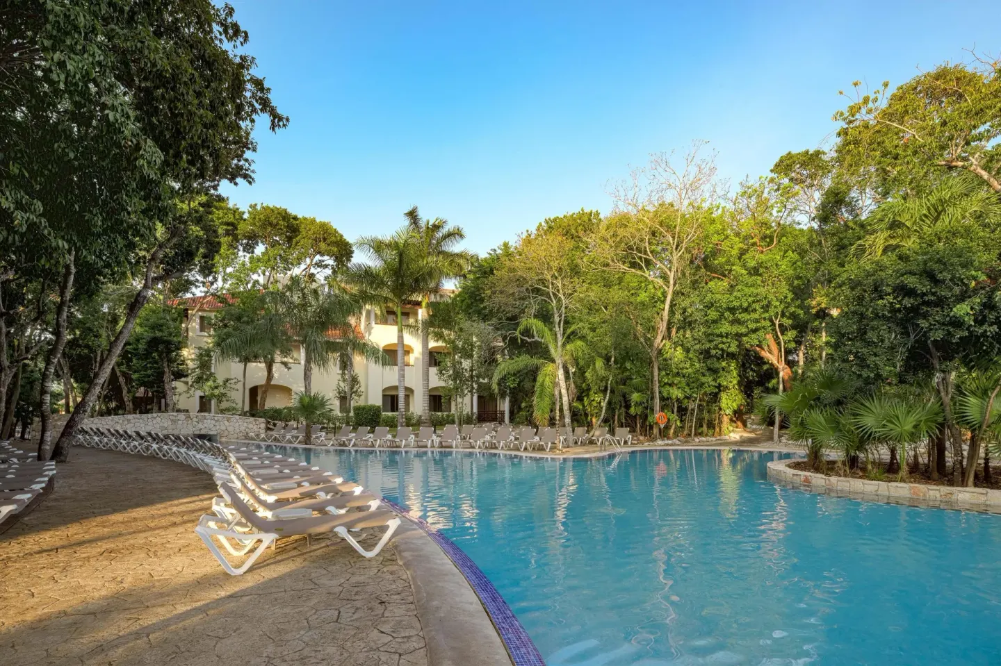 Wide pool with loungers and tropical trees at Occidental at Xcaret Destination.
