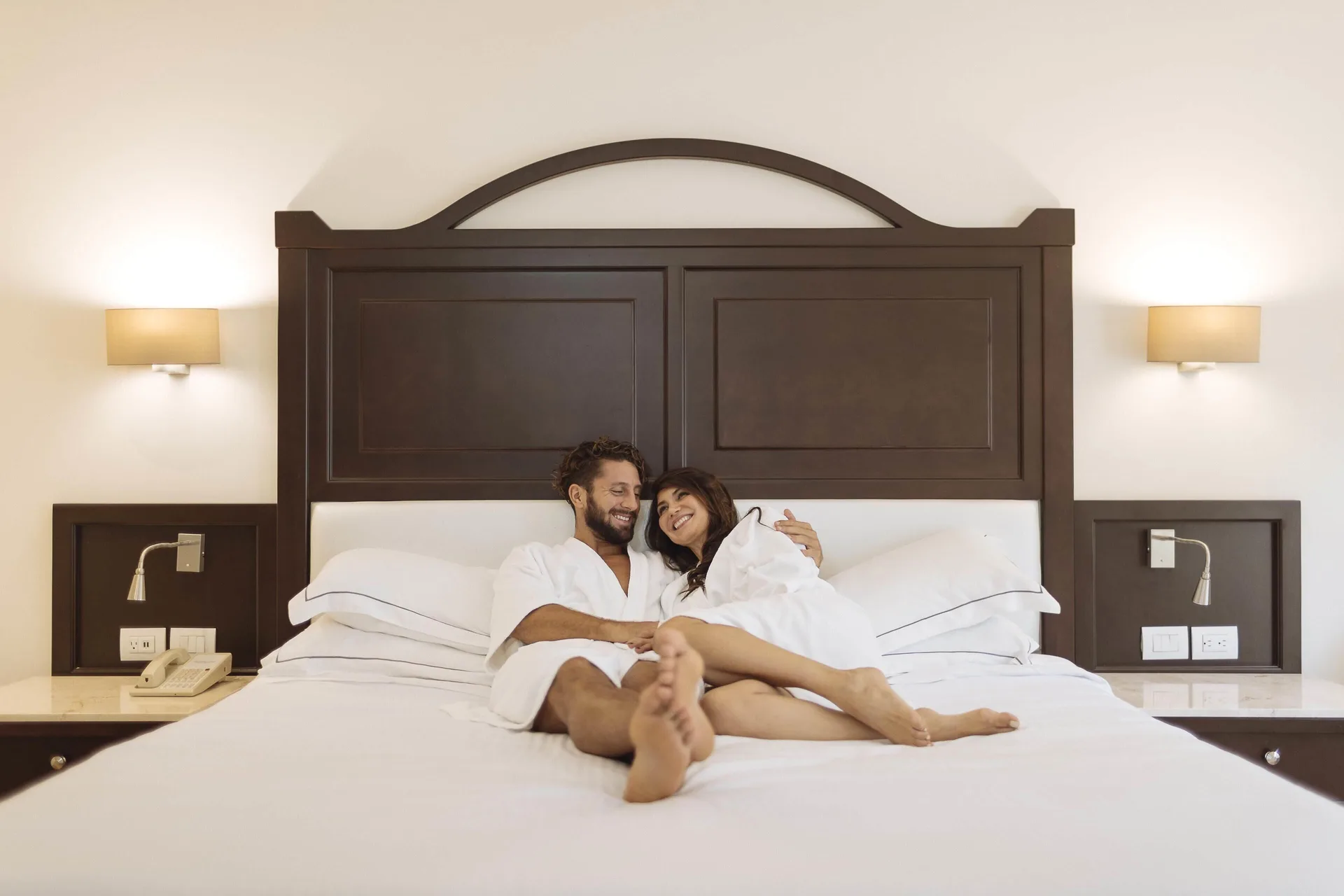 Deluxe Room king bed with guests in robes at Occidental at Xcaret Destination.