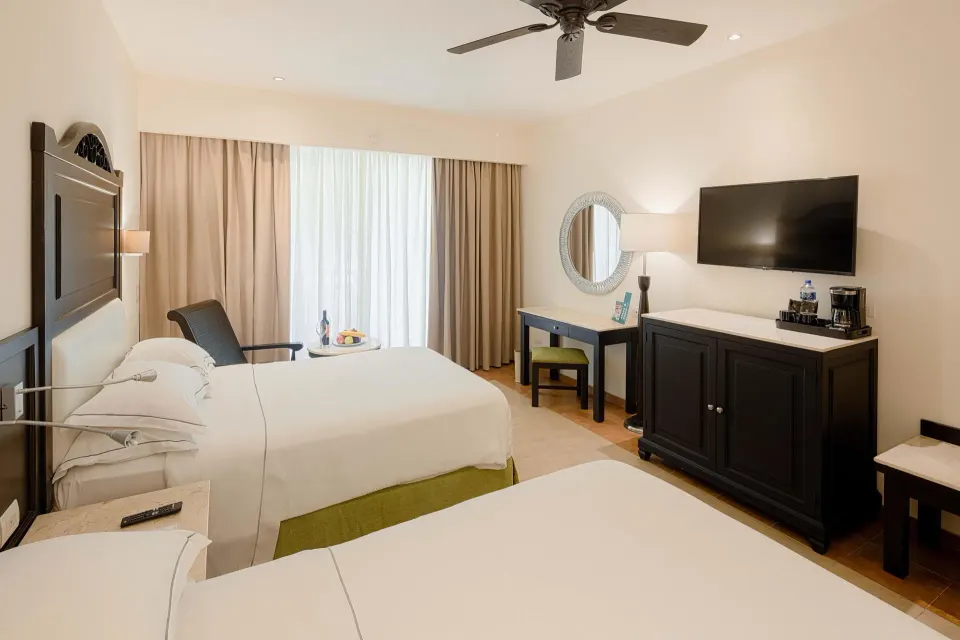 Deluxe Room with two beds, TV, desk and minibar cabinet at Occidental at Xcaret Destination.