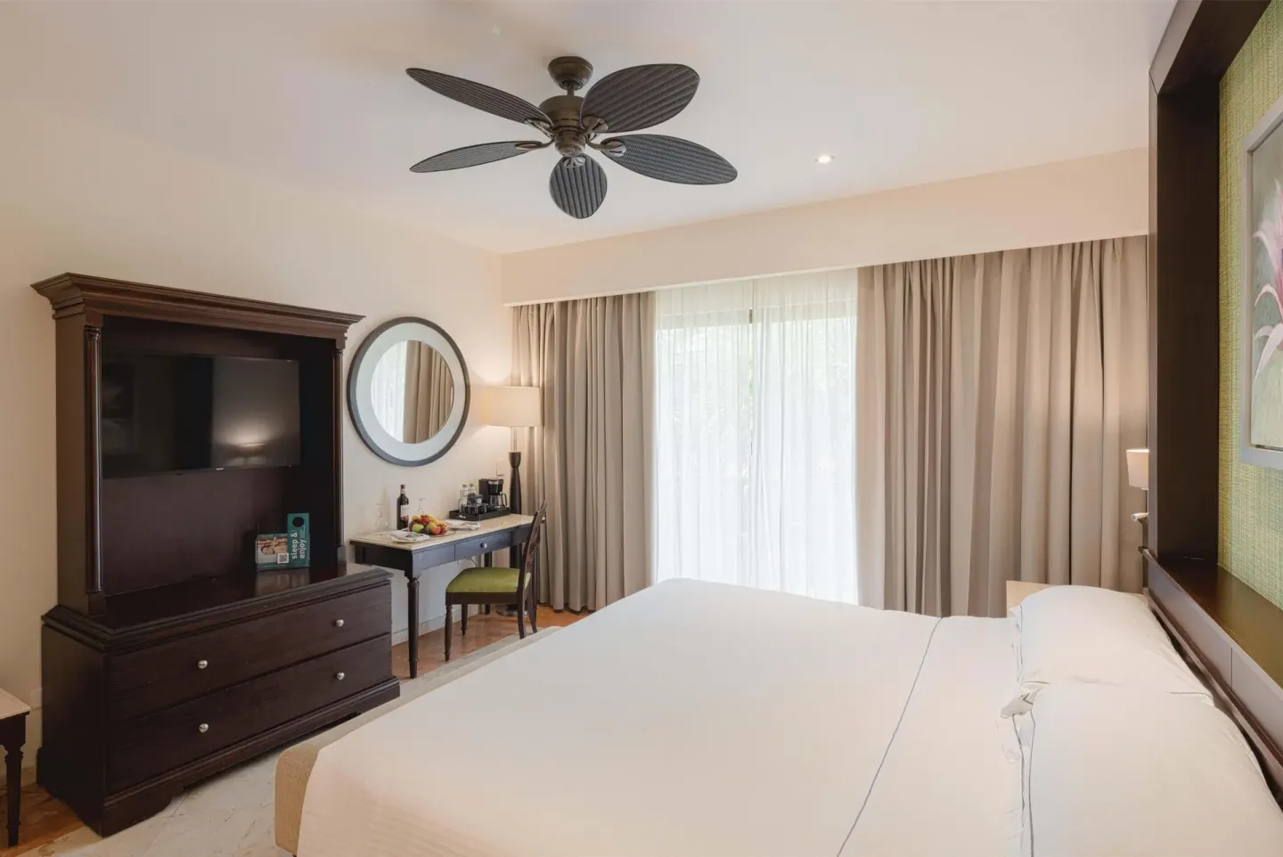 Luxury Room king bed with TV armoire, desk, and curtained balcony doors at Occidental at Xcaret Destination.