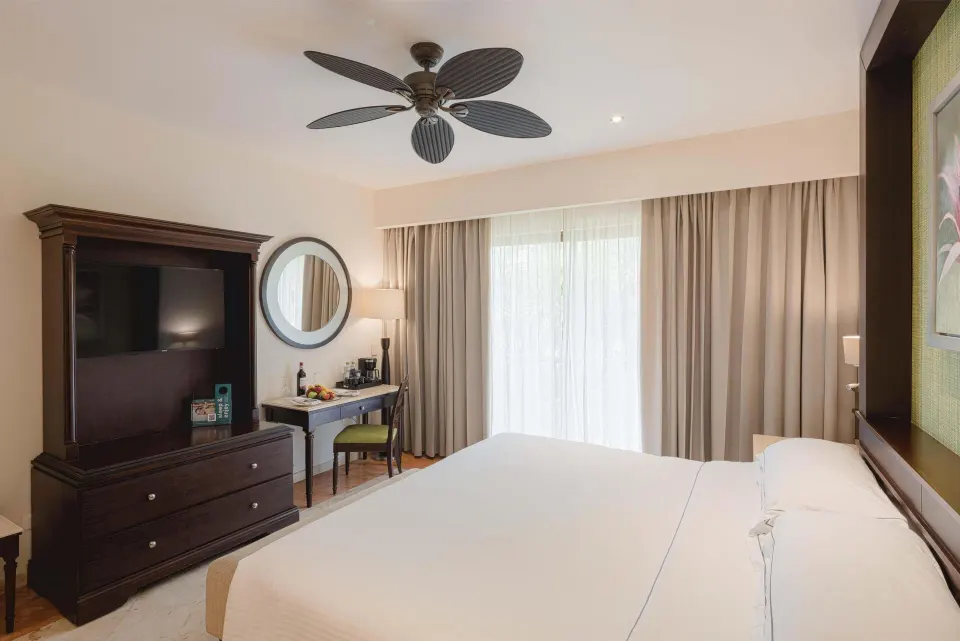 Luxury Room king bed with TV armoire, desk, and curtained balcony doors at Occidental at Xcaret Destination.