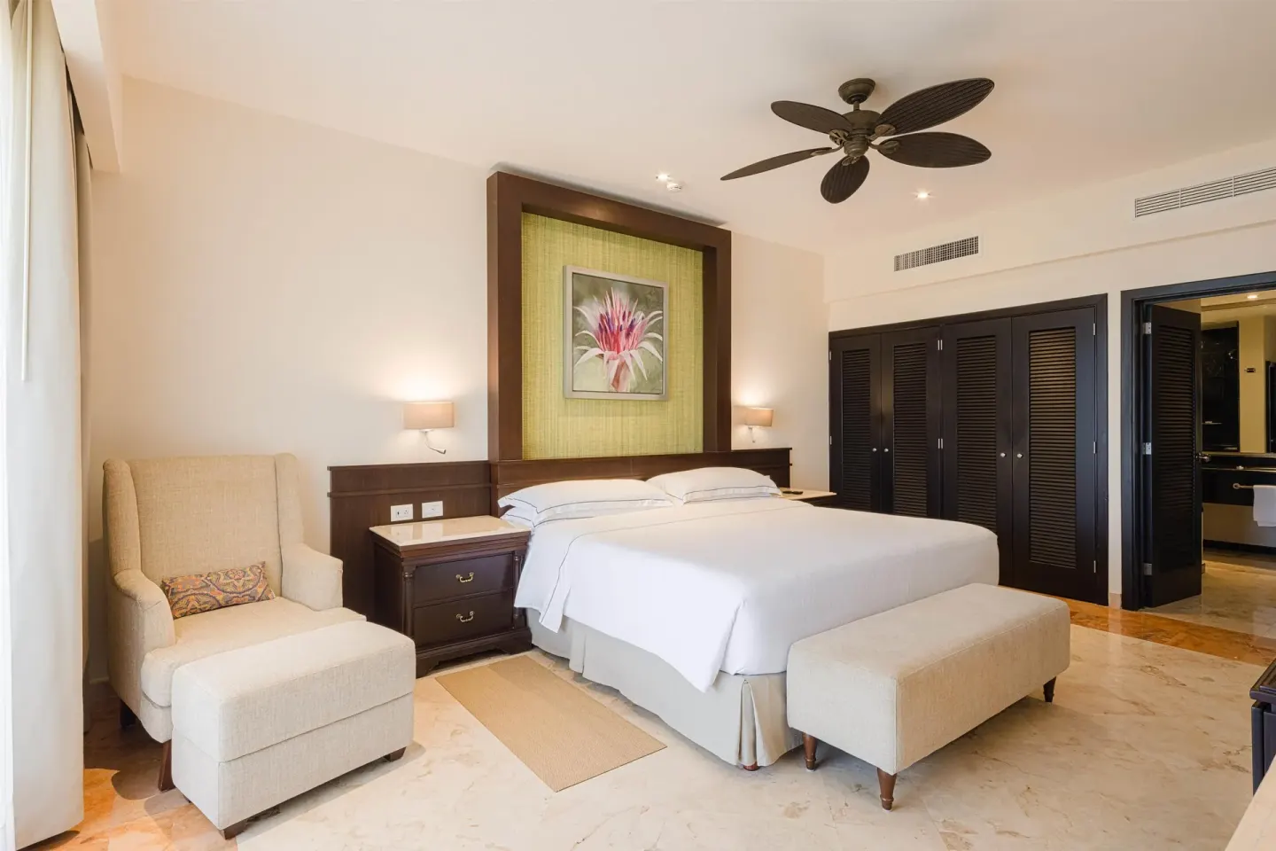 Royal Suite bedroom with king bed, lounge chair, bench and open bathroom door at Occidental at Xcaret Destination.