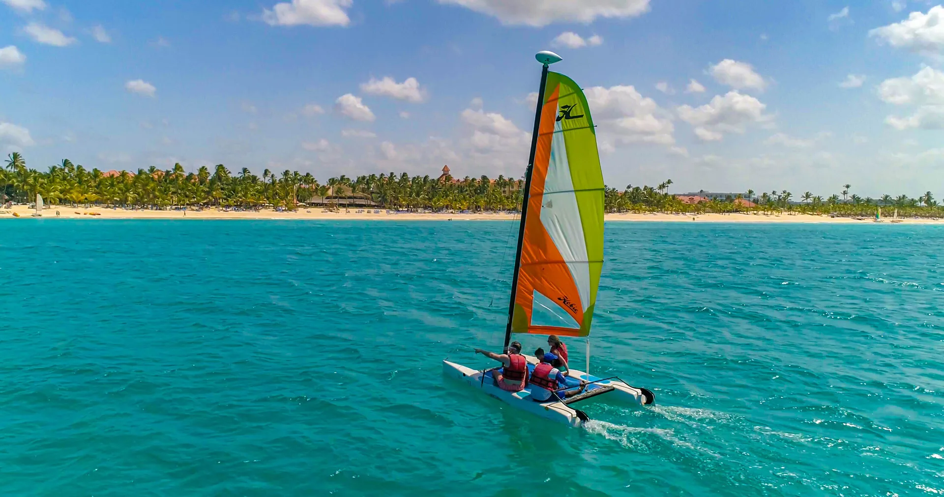 A small sailboat crosses turquoise water off the beach at Occidental Caribe.