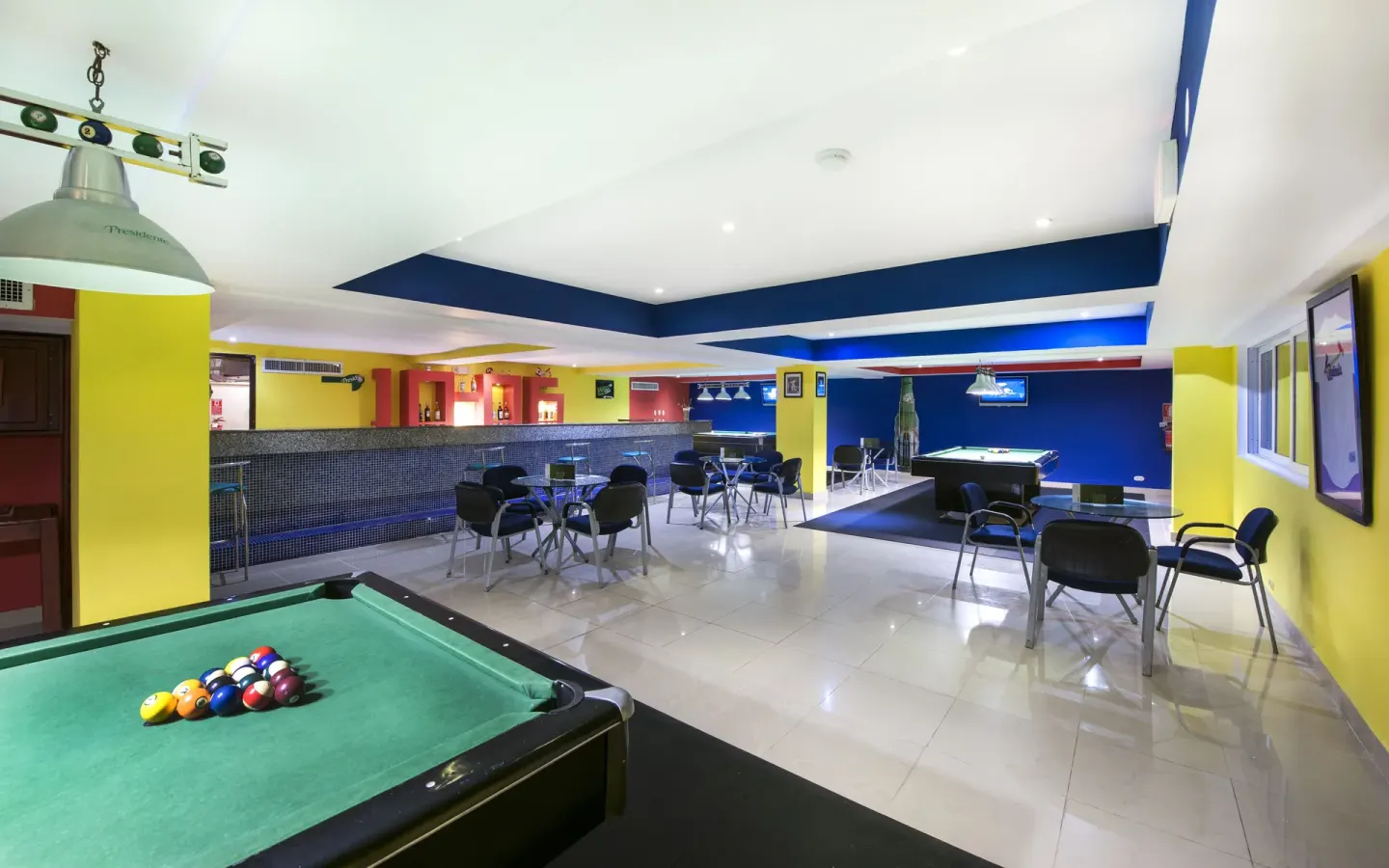 Game room with pool tables, bar seating, and bright walls at Occidental Caribe.