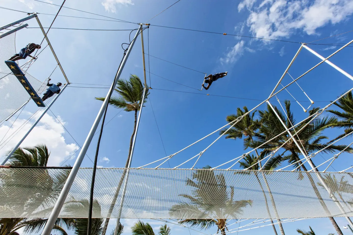 Guests fly on a trapeze rig beneath palm trees at Occidental Caribe.