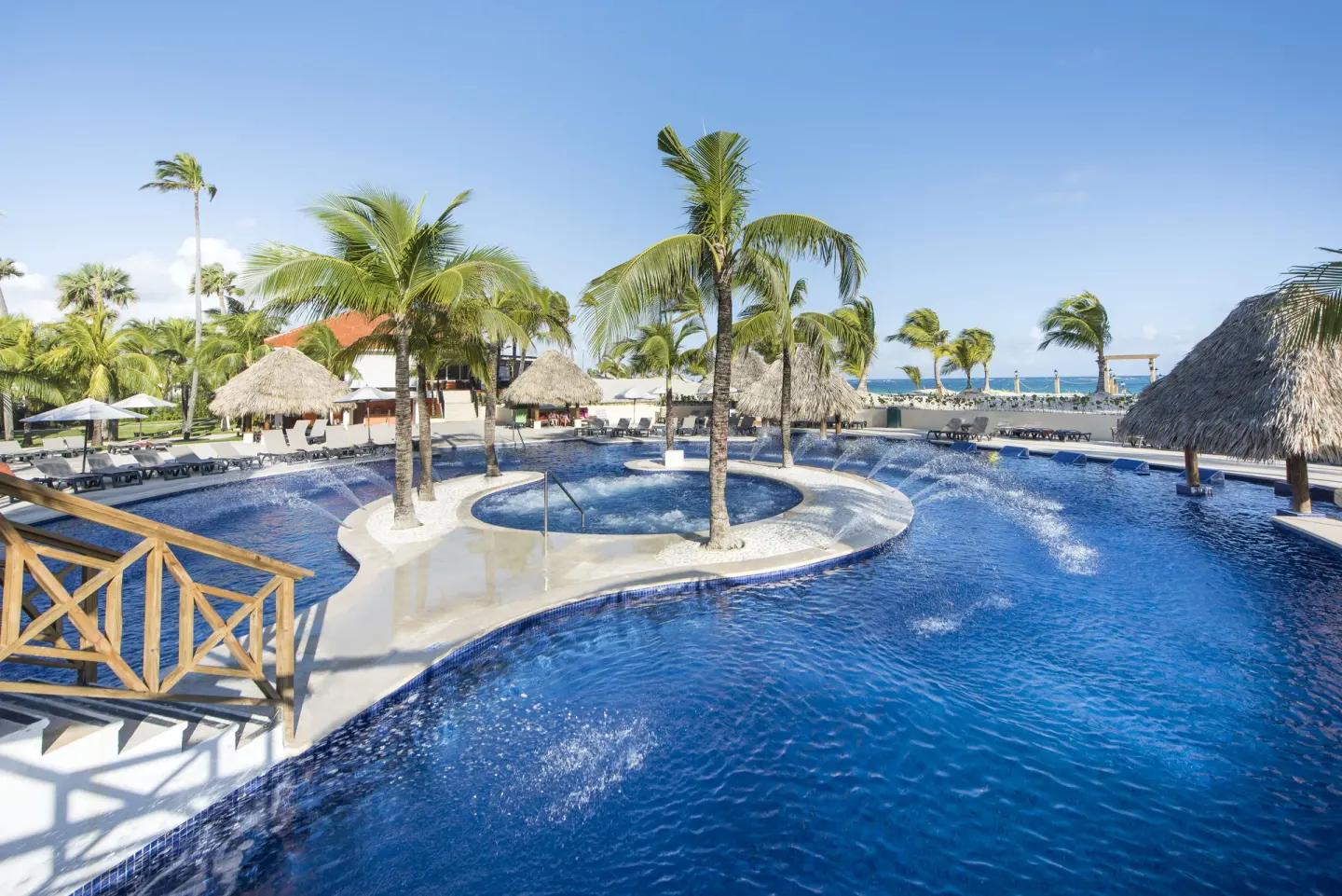 A pool with fountains, palm islands, and thatched shade areas at Occidental Caribe.