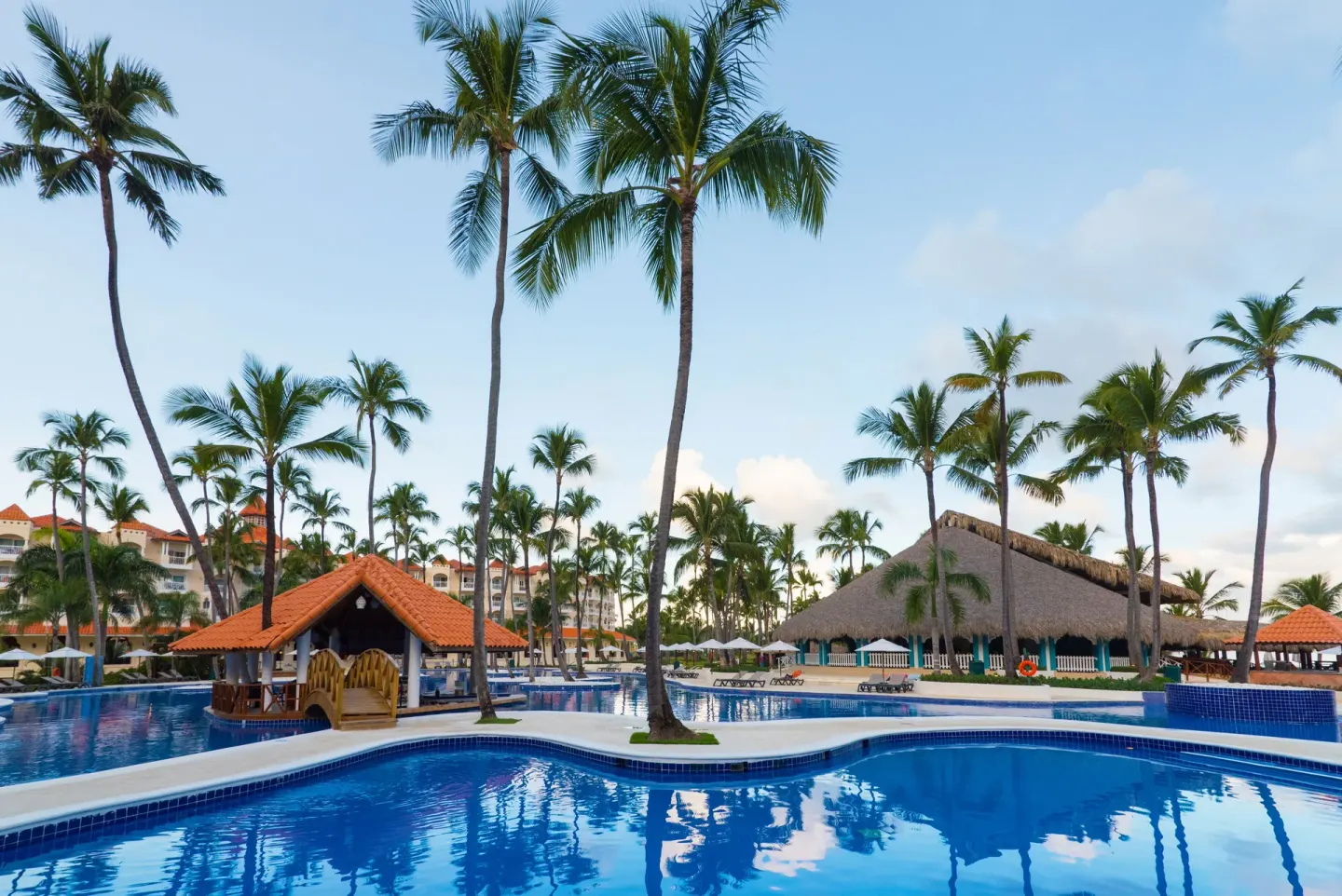 Palm trees, a small bridge, and thatched buildings border the pool at Occidental Caribe.