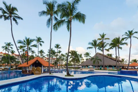 Palm trees, a small bridge, and thatched buildings border the pool at Occidental Caribe.