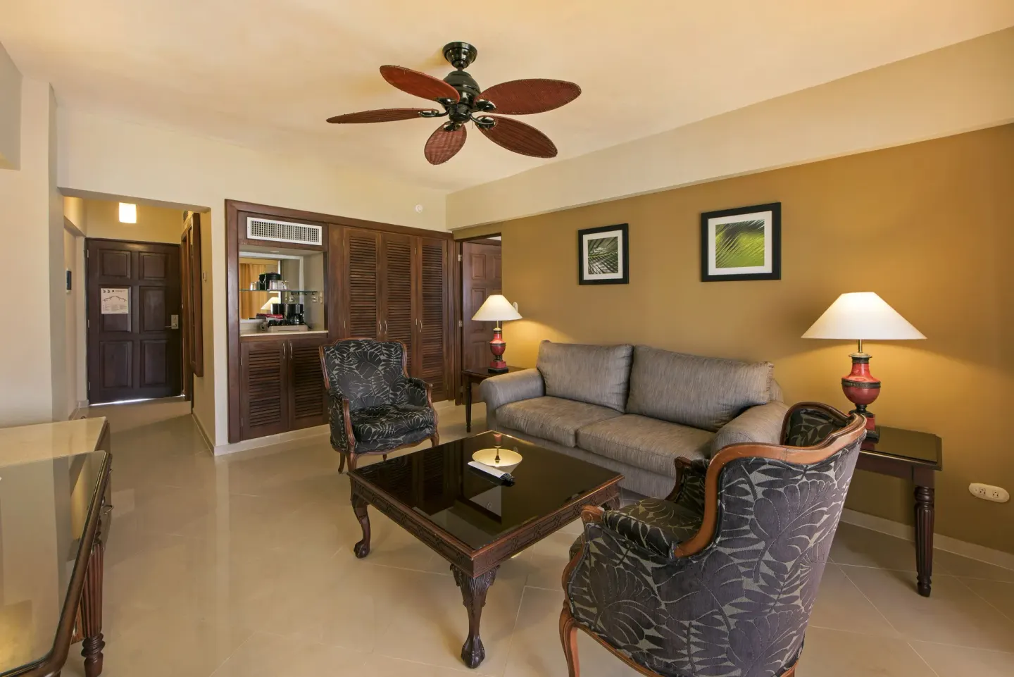 Premium Suite sitting room with gray sofa, patterned chairs, and refreshment cabinet at Occidental Caribe.
