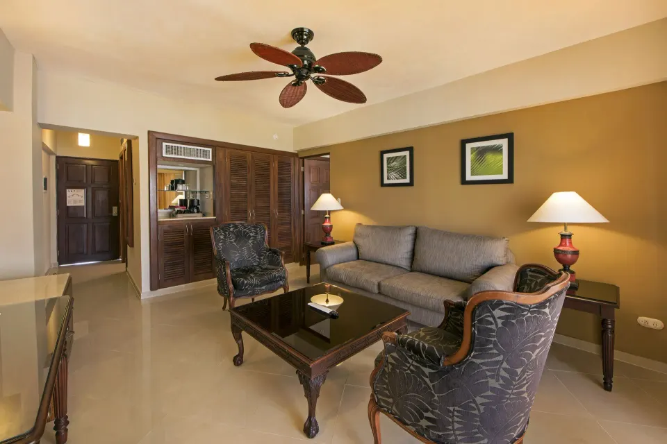 Premium Suite sitting room with gray sofa, patterned chairs, and refreshment cabinet at Occidental Caribe.