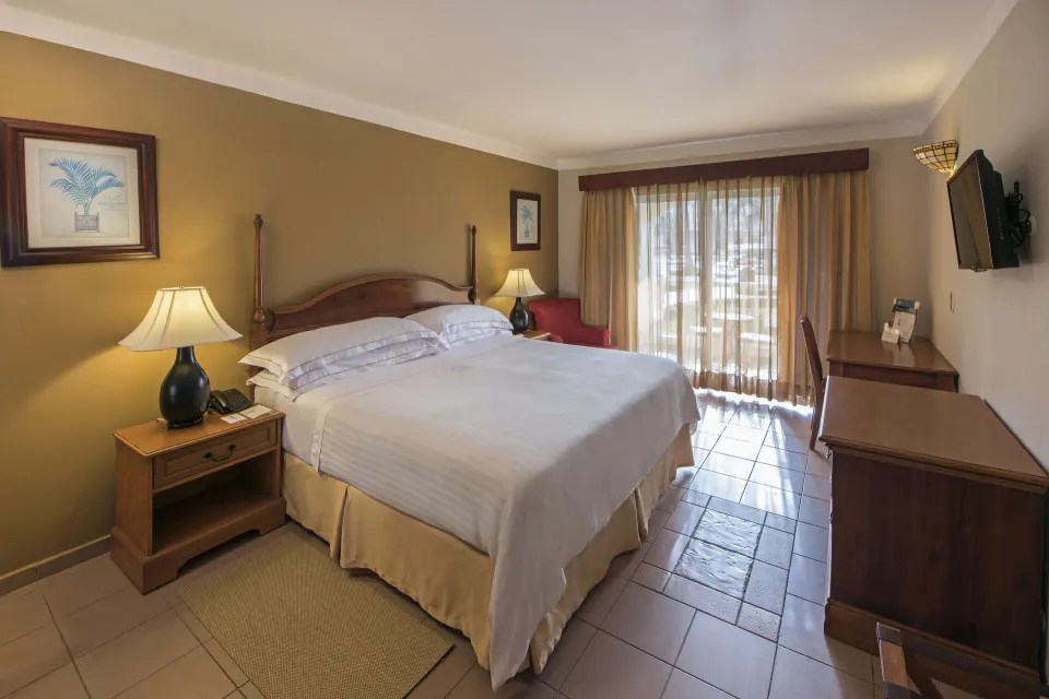 Ocean View room with a king bed, desk, TV, and balcony doors at Occidental Caribe.