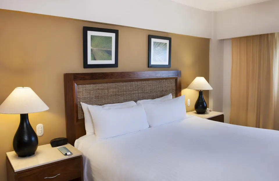 Superior Room king bed with woven headboard and lamps at Occidental Caribe.