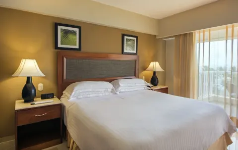 Superior Room king bed beside sheer balcony curtains at Occidental Caribe.