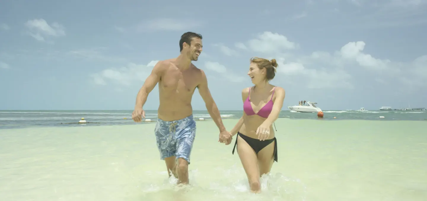 Couple walking hand in hand through shallow sea water at Occidental Costa Cancún.