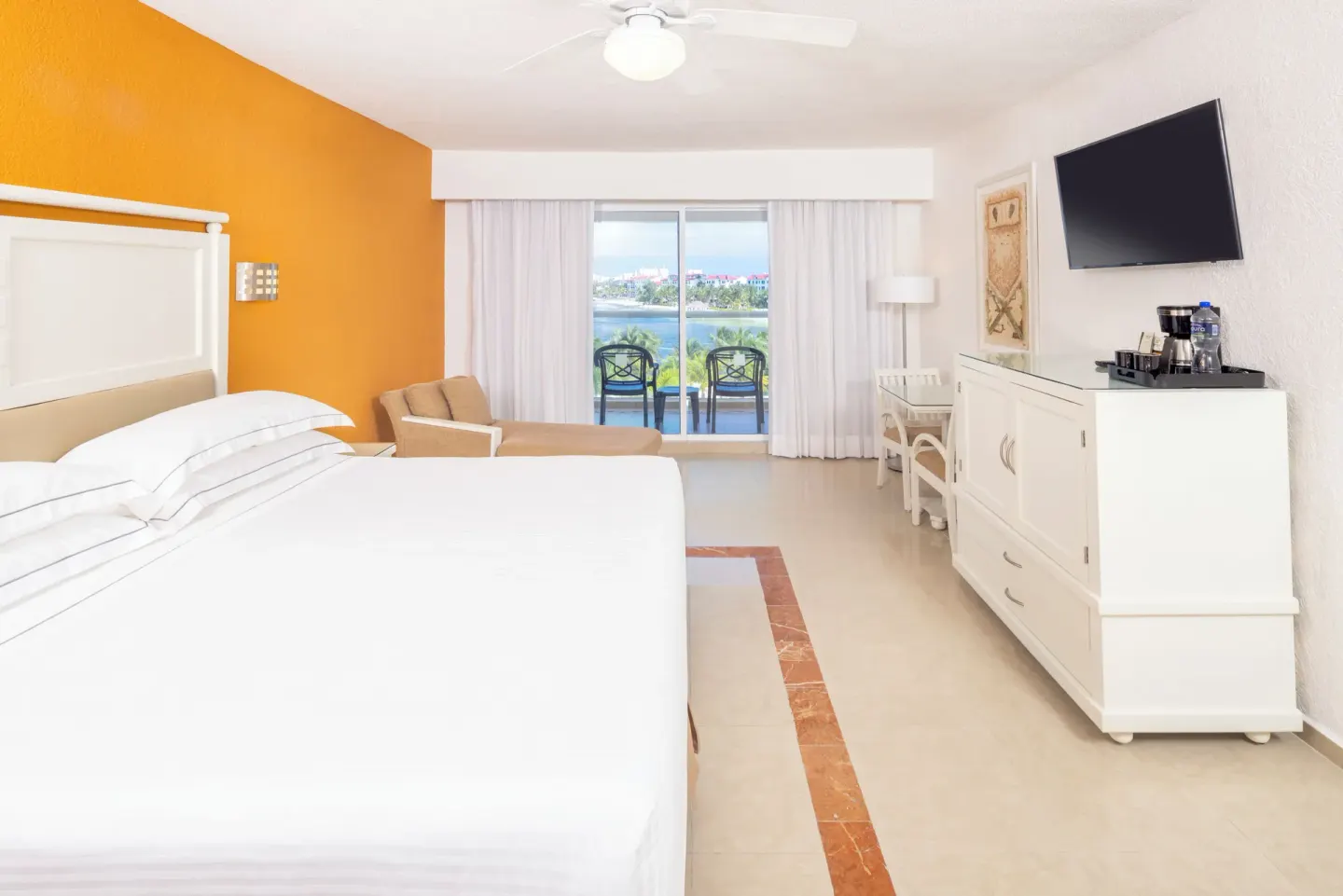 Guest room with a king bed, orange accent wall, balcony, and lagoon view at Occidental Costa Cancún.