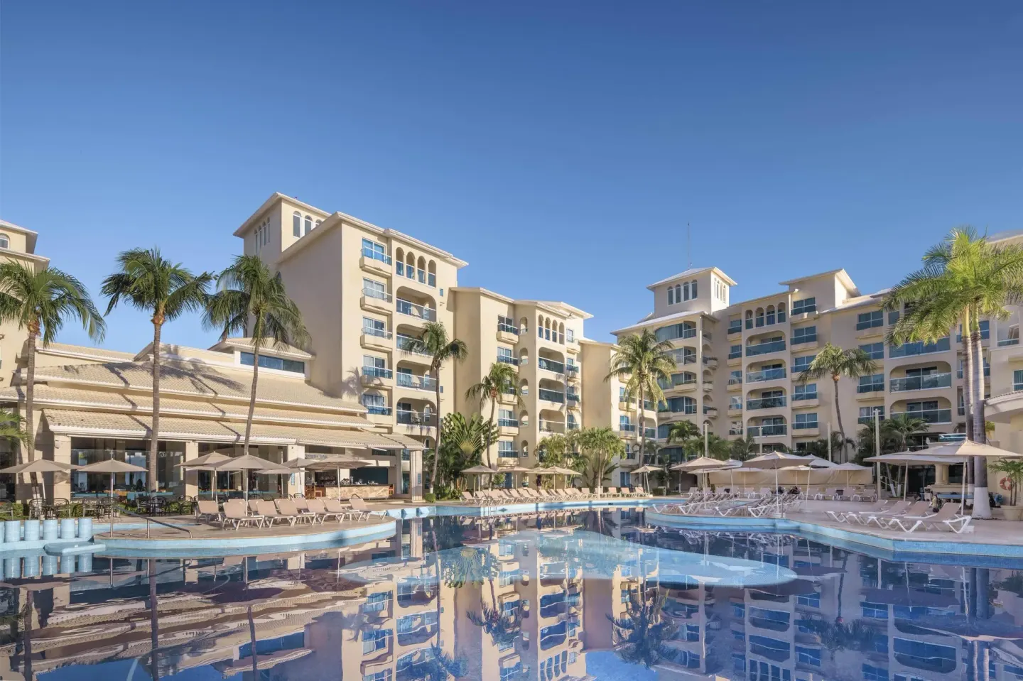 Pool deck with loungers, palms, and resort buildings at Occidental Costa Cancún.