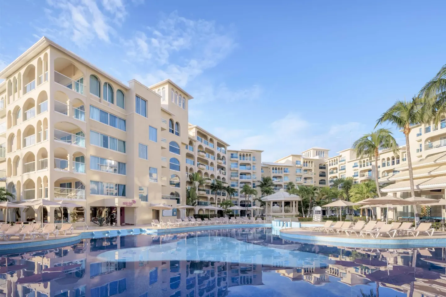 Large resort pool with arched guestroom buildings at Occidental Costa Cancún.
