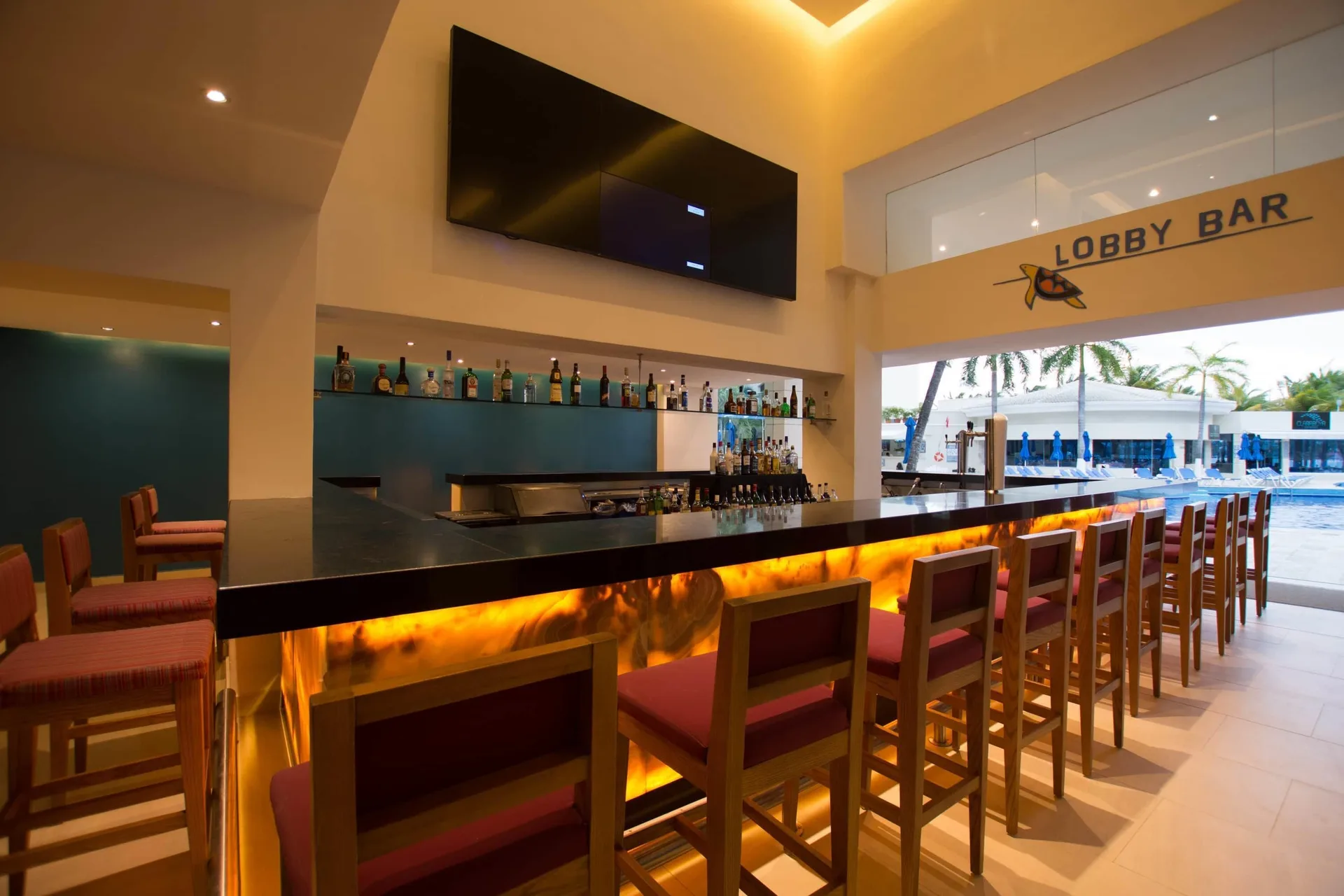 Lobby Bar counter with stools, bottles, and pool view at Occidental Costa Cancún.