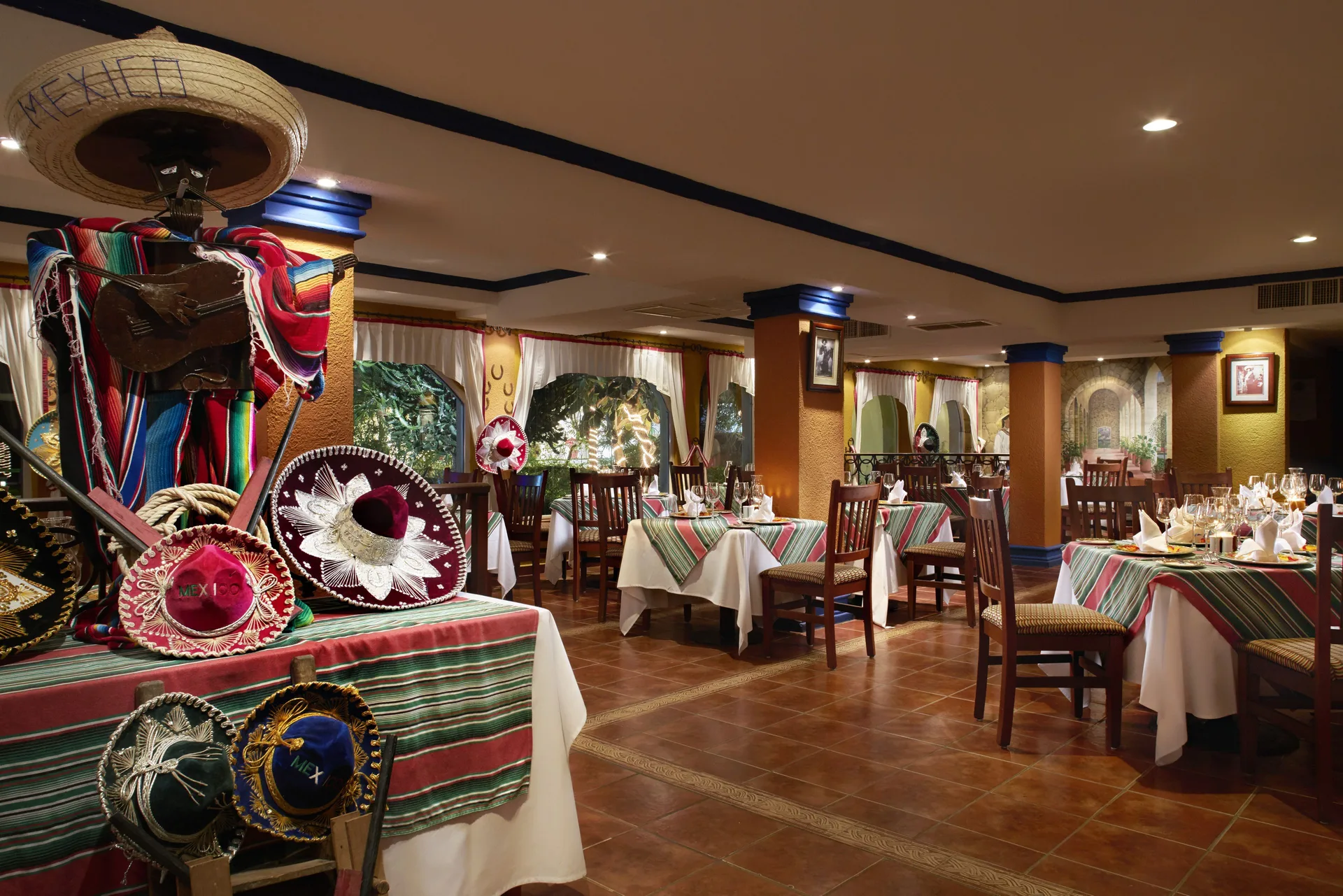 Mexican-themed dining room at Occidental Costa Cancún with sombreros, striped textiles, and set tables.