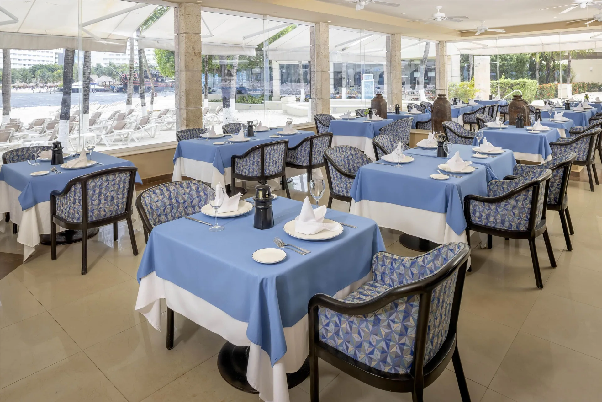 Blue tablecloth dining room at Occidental Costa Cancún with windows overlooking poolside loungers.