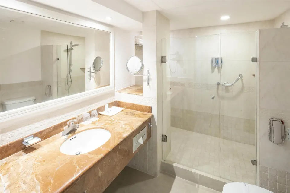 Guest room bathroom with marble vanity and glass shower at Occidental Costa Cancún.