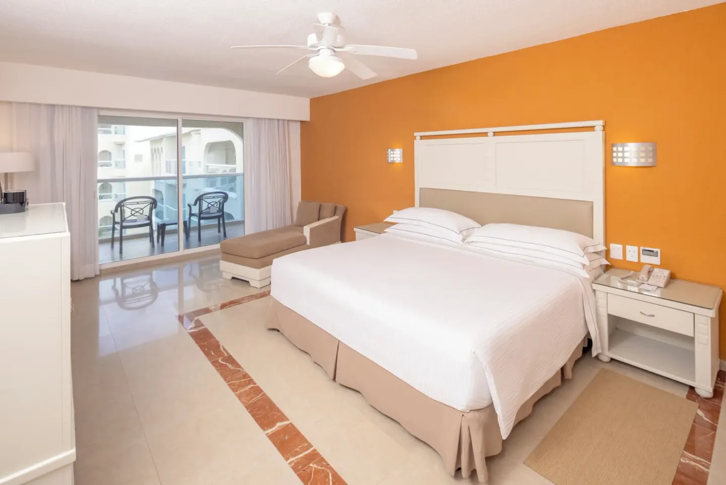King bed guest room with orange wall and terrace seating at Occidental Costa Cancún.