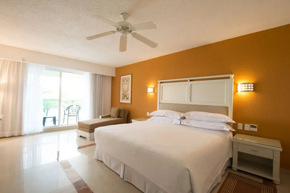 King bed guest room with balcony seating and chaise lounge at Occidental Costa Cancún.