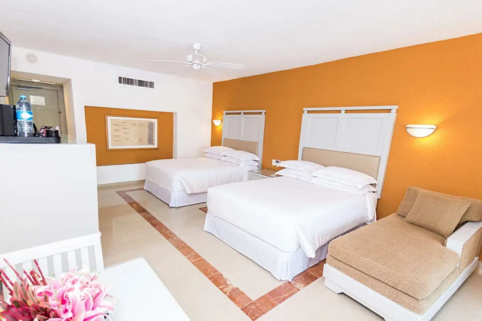 Two-bed guest room with chaise lounge and wall-mounted TV at Occidental Costa Cancún.