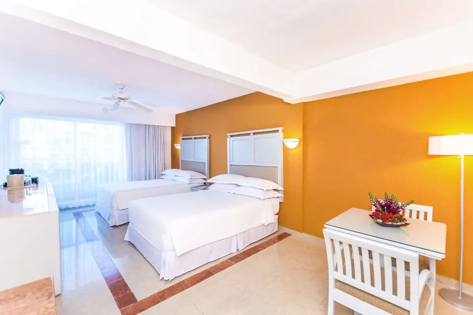 Two-bed guest room with orange accent wall and table at Occidental Costa Cancún.