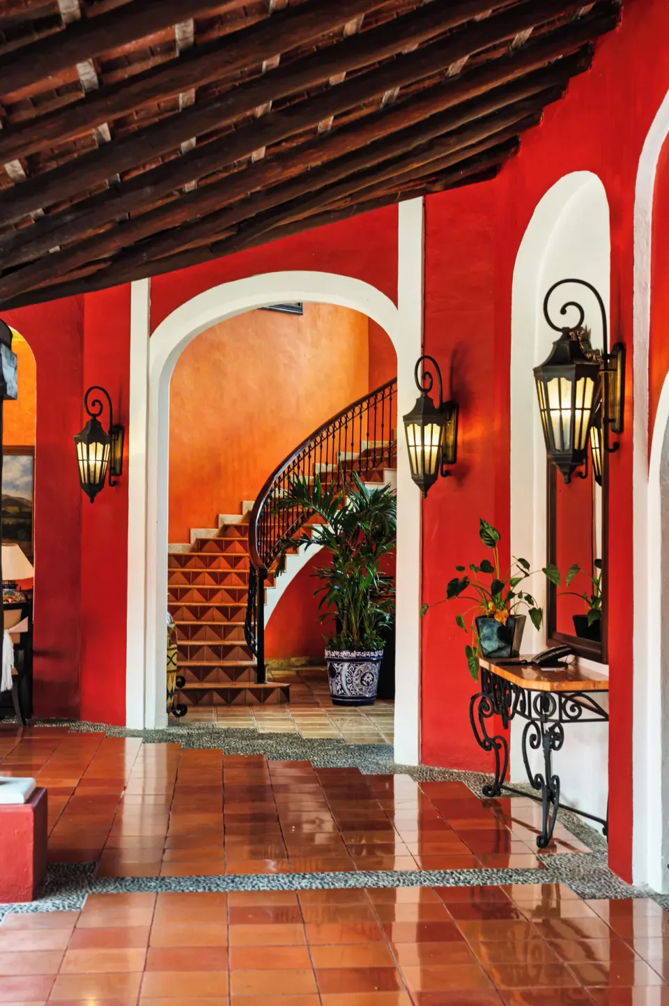 Red lobby corridor with arches, lanterns, and a curved staircase at Occidental Cozumel.