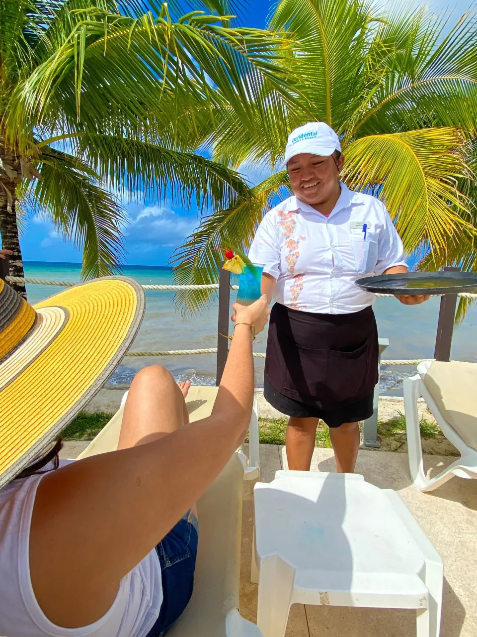Server handing a tropical drink to a beach lounger guest at Occidental Cozumel.