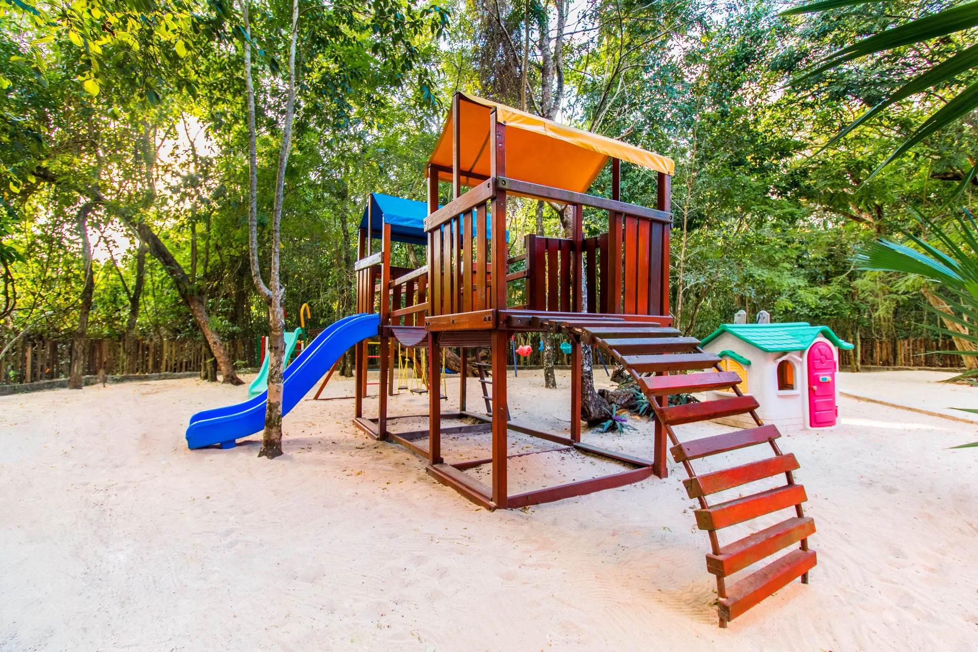 A children’s playground with slides sits on sand among trees at Occidental Cozumel.