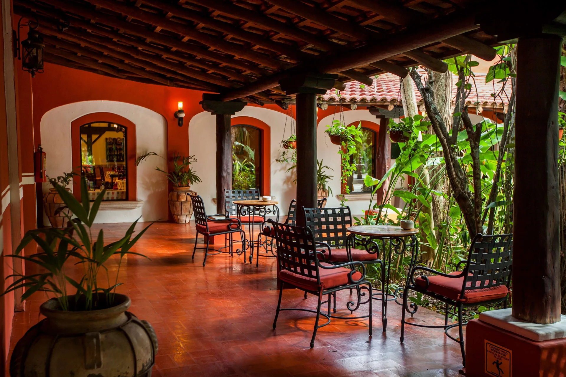 Covered terrace with tables, red cushions, and tropical plants at Occidental Cozumel.