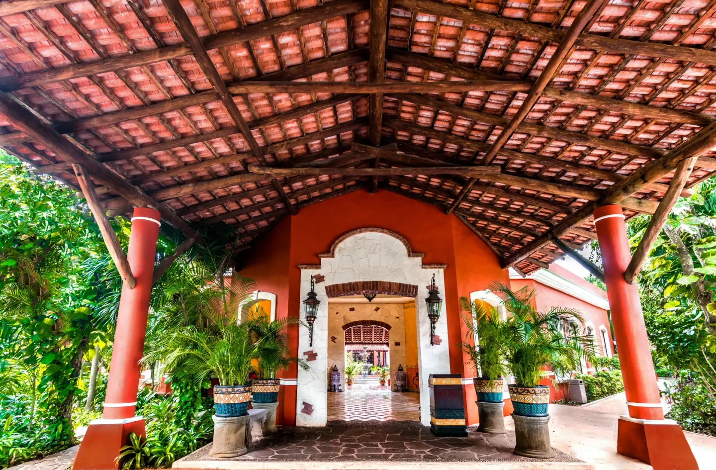 Covered resort entrance with red columns and tropical plants at Occidental Cozumel.