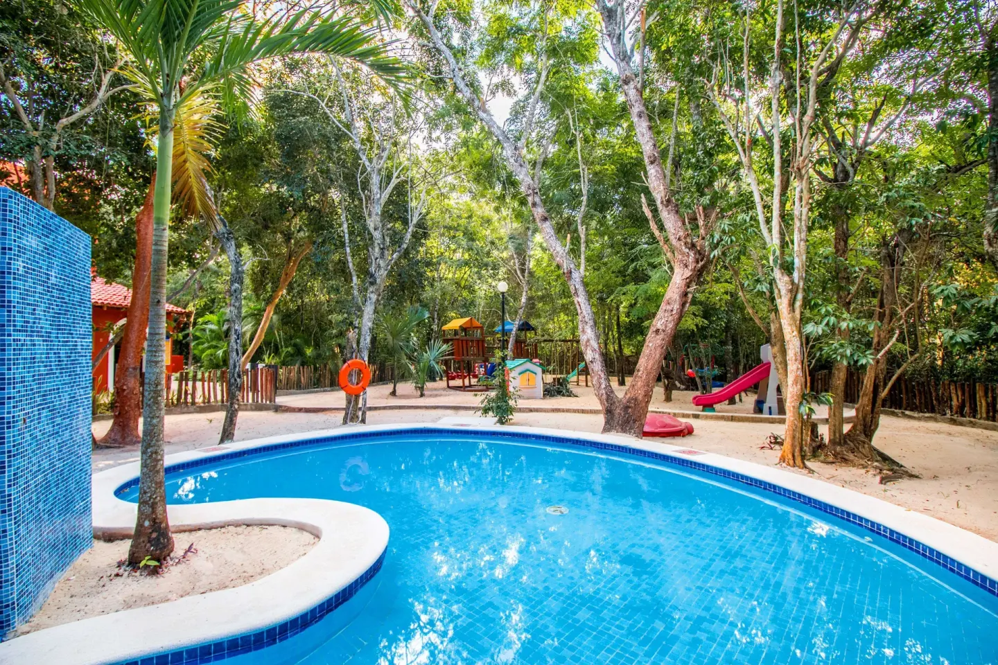 Curved pool beside a children’s play area in the trees at Occidental Cozumel.