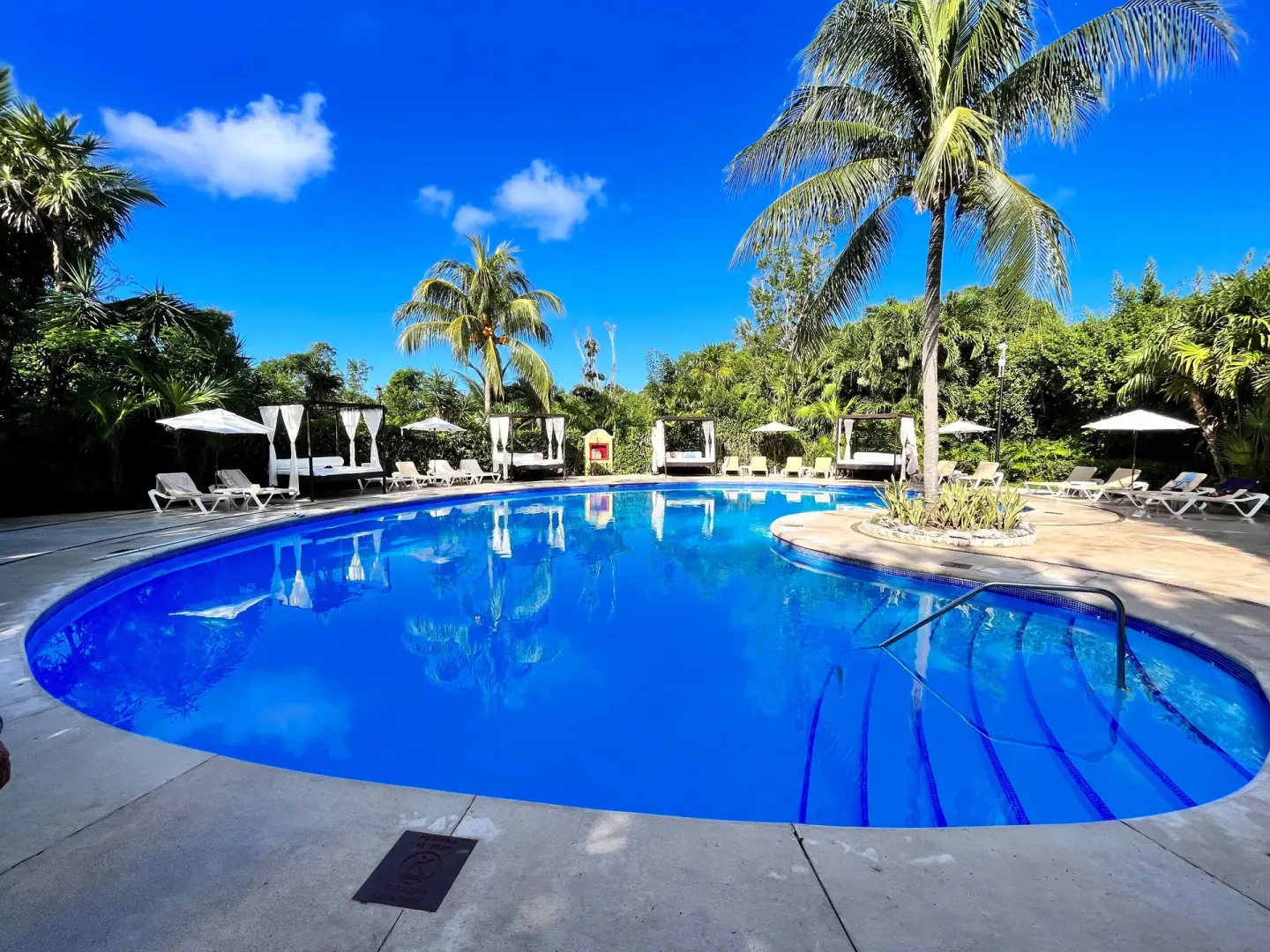 Blue resort pool with loungers, cabanas, and palm trees at Occidental Cozumel.