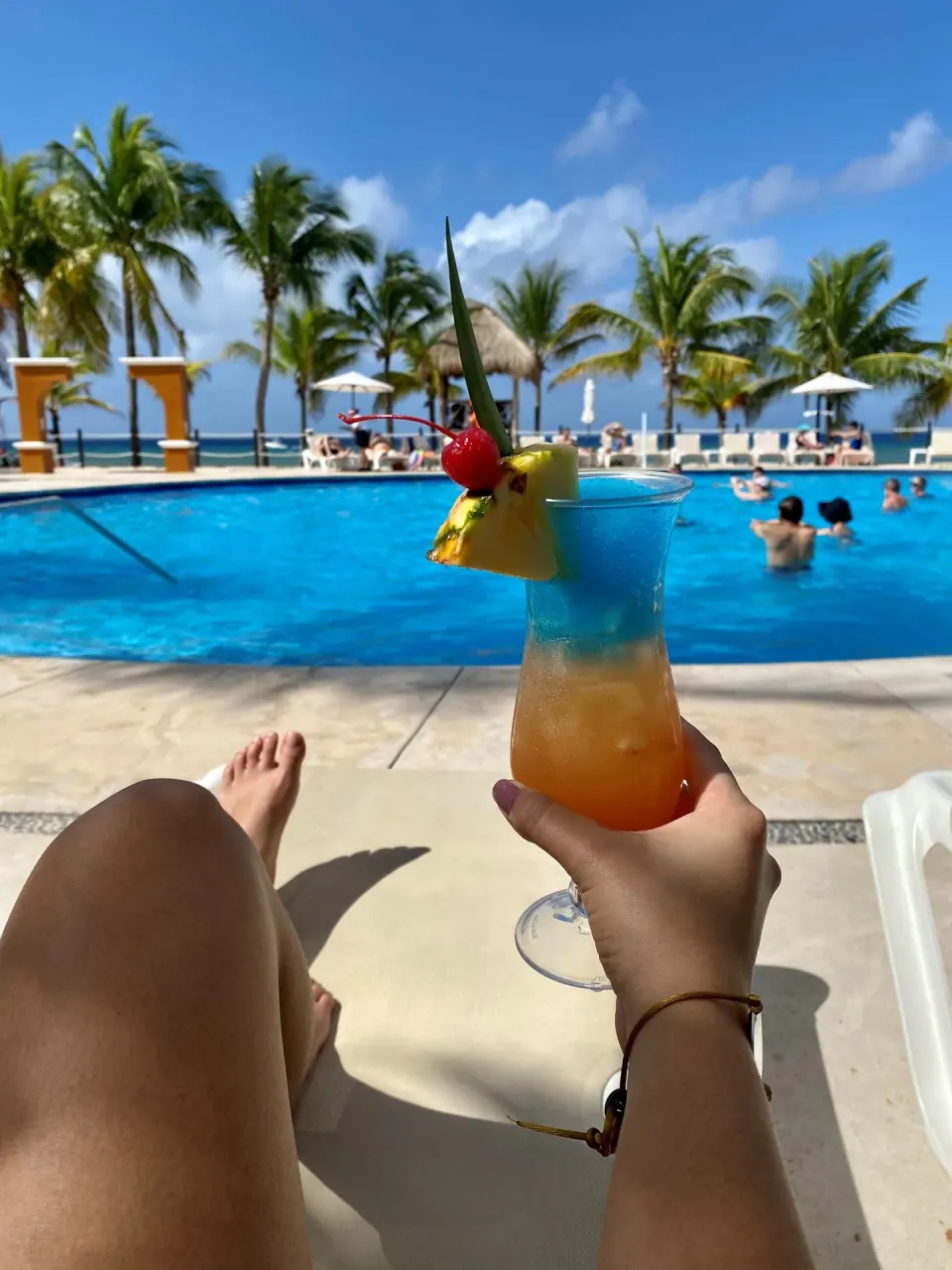Hand holding a fruit-garnished drink beside the pool at Occidental Cozumel.