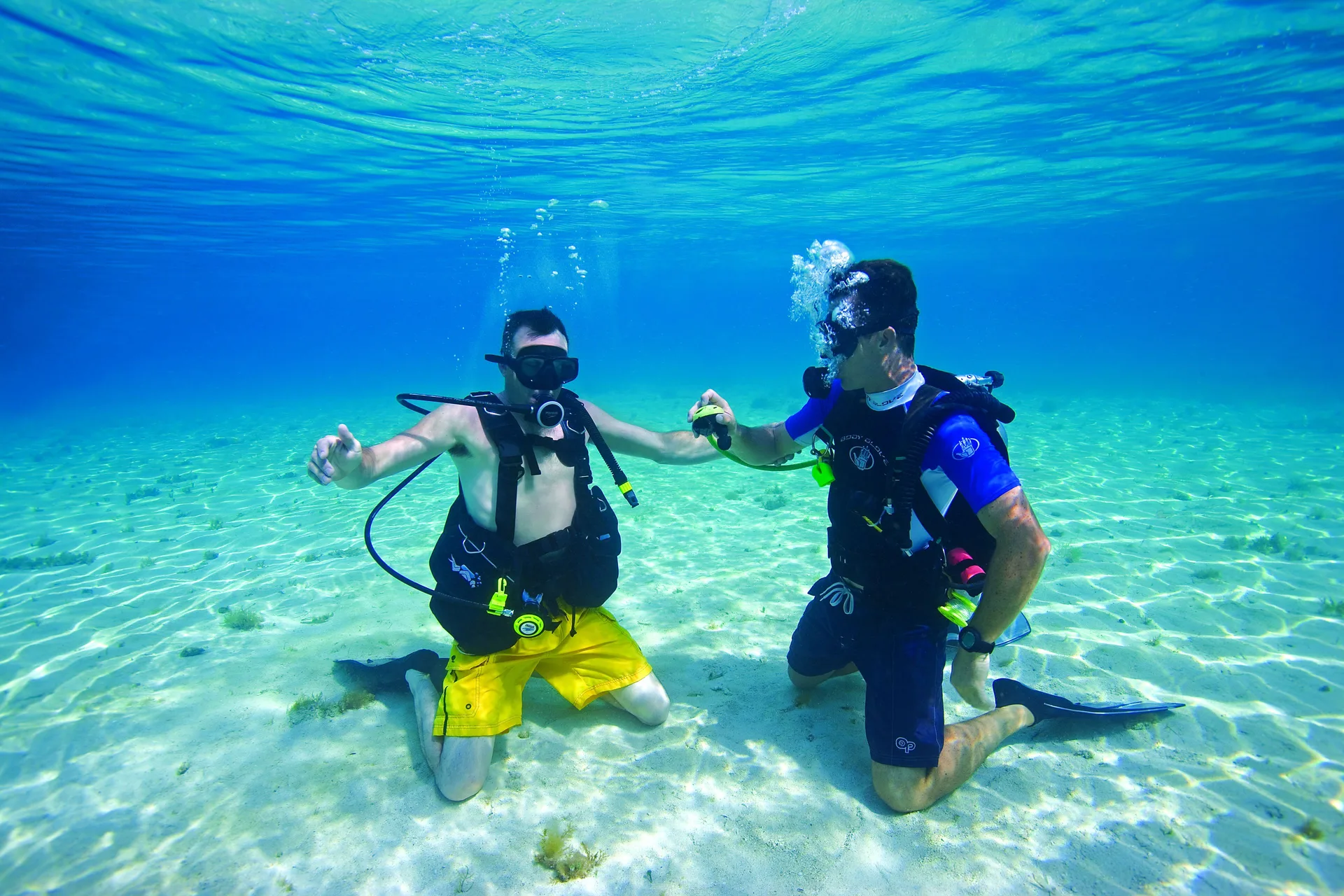 Two scuba divers kneeling on a sandy seabed in clear water at Occidental Cozumel.