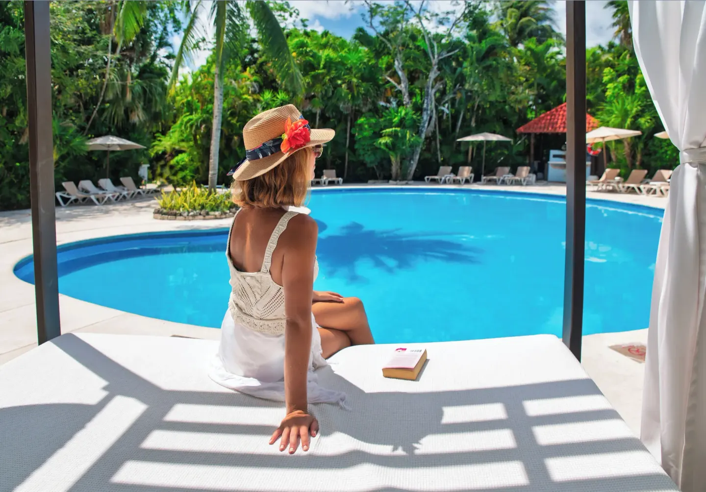 Guest seated on a shaded daybed beside a garden pool at Occidental Cozumel.
