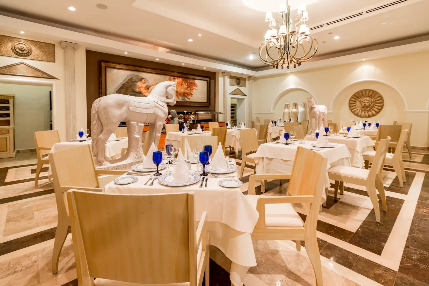 An elegant dining room with white horse sculptures and blue glasses at Occidental Cozumel.