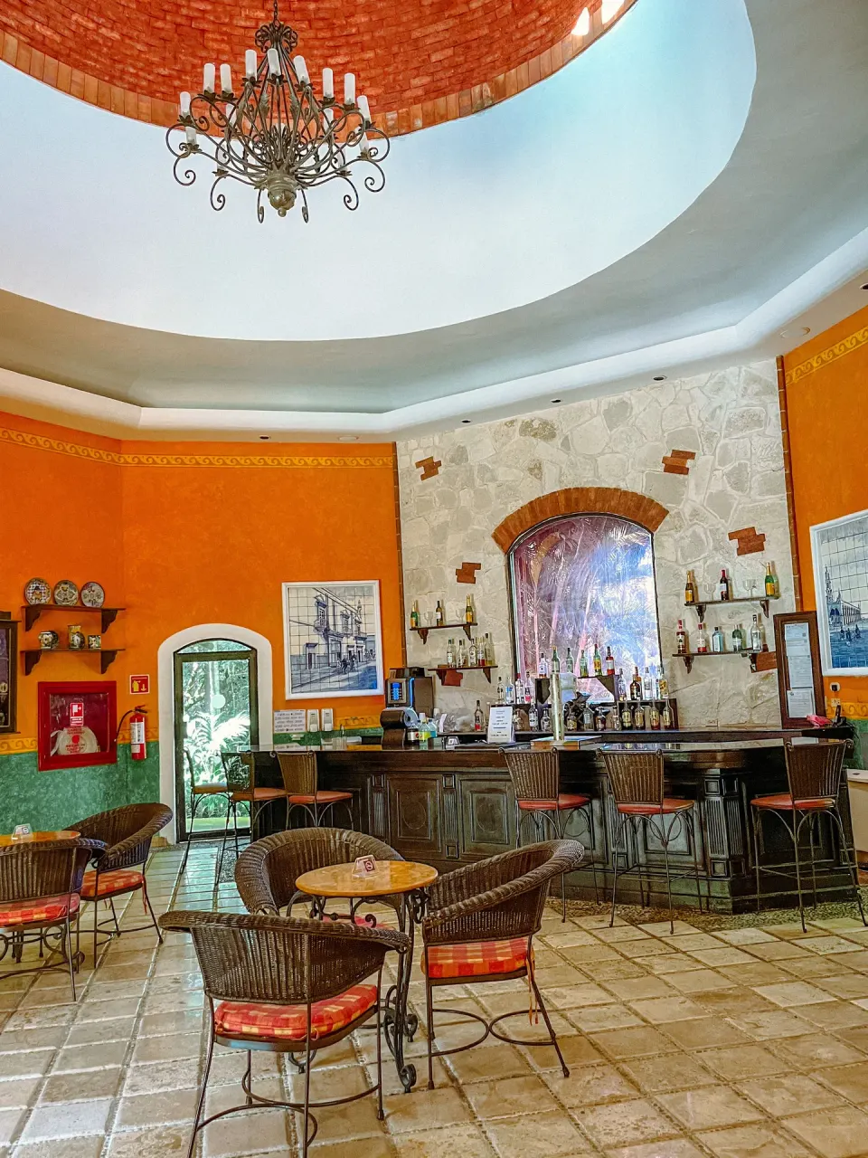 Bar with wicker seating, orange walls, and a chandelier at Occidental Cozumel.