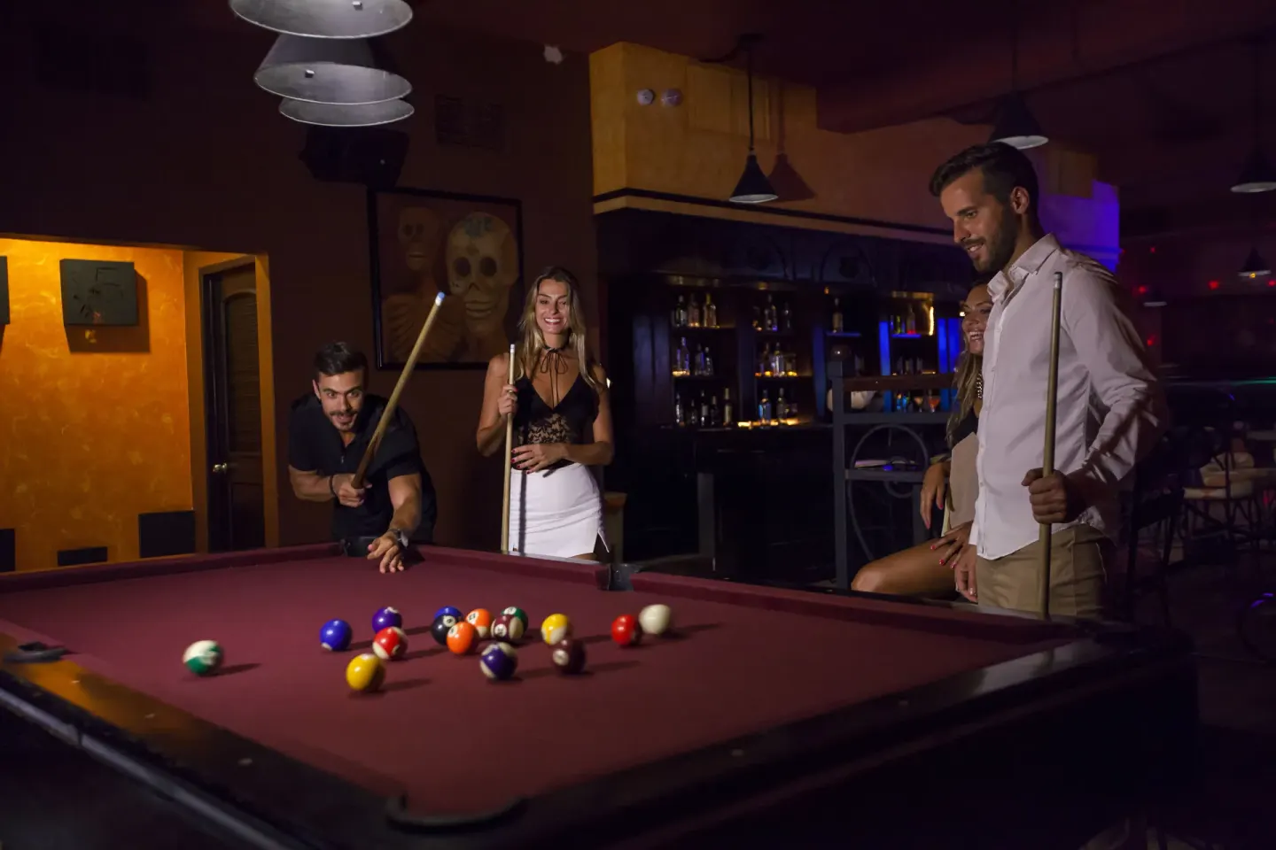 Guests play pool in a dim bar game room at Occidental Cozumel.